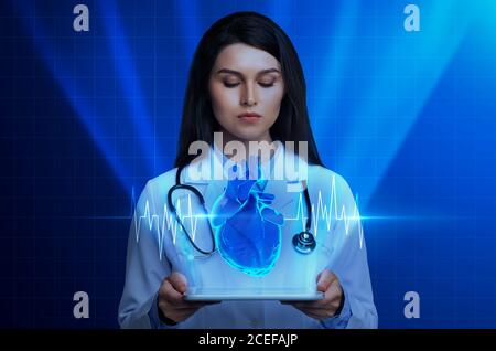 Femme médecin tenant une tablette numérique avec hologramme cardiaque Banque D'Images