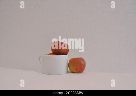 Pommes rouges, dans une tasse de café en céramique blanche, pleine, avec une pomme sur le côté, photo conceptuelle, fond blanc, Brésil, Amérique du Sud Banque D'Images