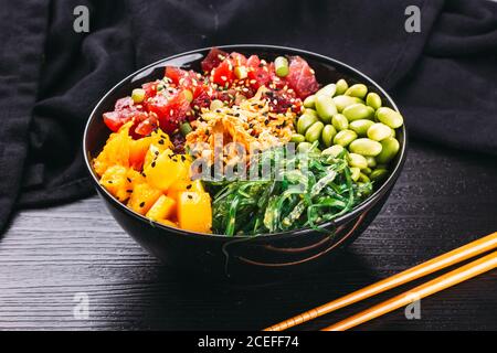 Bol en céramique avec assortiment de plats asiatiques sur fond noir plan d'examen en bois près des baguettes et de la sauce soja Banque D'Images