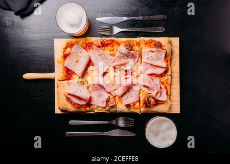 Ensemble élégant de boissons dans des verres et couverts disposés autour planche à découper en bois avec hors-d'œuvre de pizza cuite avec sauce et tranches de jambon sur une table en bois foncé Banque D'Images