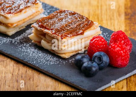 Gros plan de pâtisseries avec garniture à la crème et au caramel planche avec baies fraîches Banque D'Images