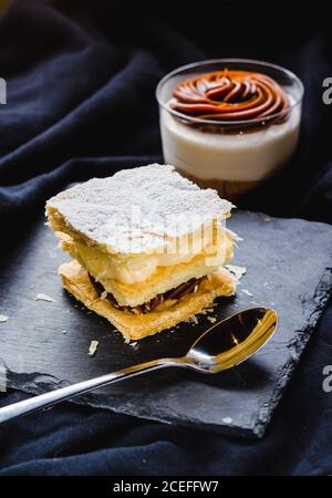 Gros plan d'une pâte feuilletée avec crèmes sur l'assiette et dessert dans une tasse composée de textile doux. Banque D'Images