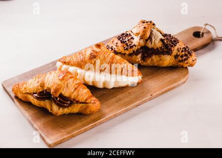 Planche en bois avec trois croissants farcis de diverses et délicieuses crèmes sur la surface blanche. Banque D'Images