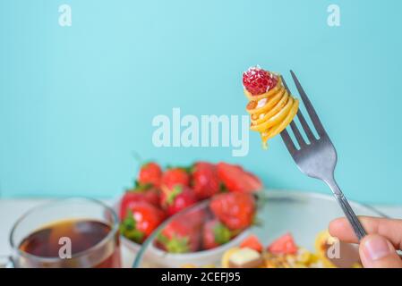 petites crêpes à la fourchette avec fraises fraîches, banane, chocolat, noix de coco et miel dans une assiette sur fond bleu. tendance alimentaire 2020. Banque D'Images