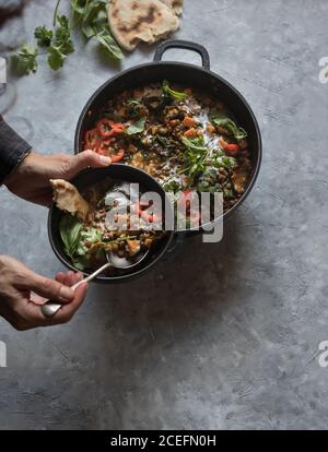 Personne tenant le bol près du pot avec ragoût de lentilles et curry de patates douces Banque D'Images