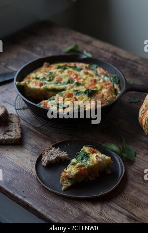 Assiette et casserole en métal avec de délicieux frittata de citrouille et d'épinards debout sur un plan d'examen en bois Banque D'Images