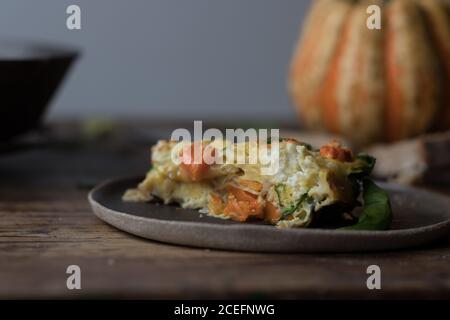 Gros plan d'un morceau de délicieux frittata à la citrouille et aux épinards posé sur une plaque sur un plan d'examen en bois Banque D'Images