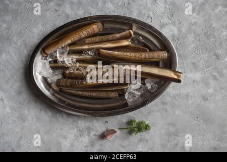 De dessus la prise d'ail et d'herbe couché près du métal assiette avec glaçons et palourdes fraîches sur plâtre surface Banque D'Images