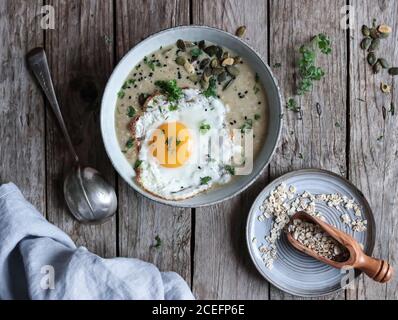 Du dessus de la prise de bol de porridge de grain délicieux avec œufs et miso frits savoureux et herbes sur bois plan d'examen Banque D'Images