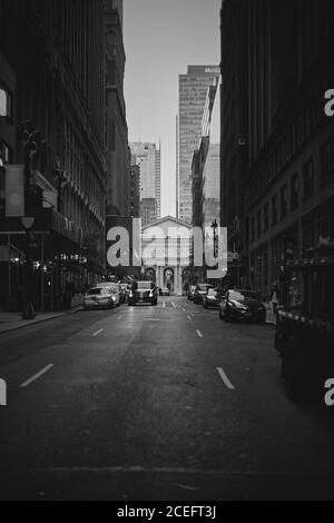 Photo en noir et blanc de voitures garées et en voiture dans la rue entre les gratte-ciel de New York. Banque D'Images