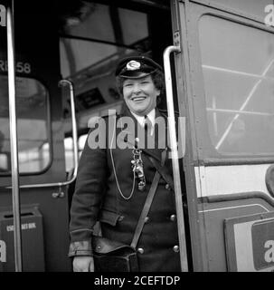 Une conductrice du bus à Fife, en Écosse, sourit alors qu'elle se trouve à l'arrière de son bus routemaster dans les années 1950, avant qu'elle sonne la cloche pour signaler que le conducteur peut conduire Banque D'Images