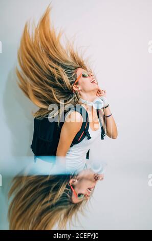 Vue latérale d'une jeune jolie femme en haut blanc avec un sac à dos dansant en studio et riant sur fond blanc Banque D'Images