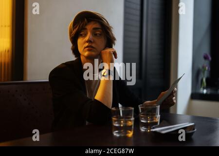 Jeune jolie femme au Cap assise seule à table dans un restaurant moderne et lisant le menu Banque D'Images