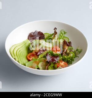 De magnifiques concombres, tomates et potherbs hachés mélangés dans un grand bol en céramique blanc sur fond blanc Banque D'Images