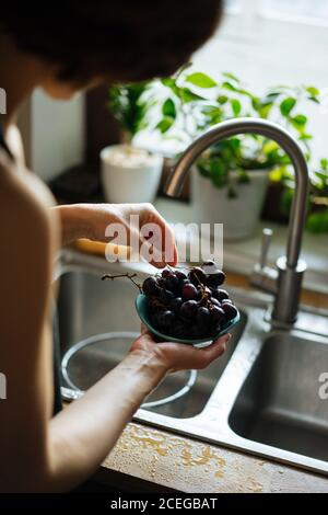 Rognez les mains des femmes en tenant la crépine métallique avec des fraises à raisins brillants sous l'évier, tapez sur le comptoir en bois par le dessus Banque D'Images