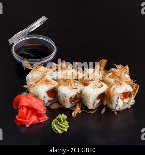 Un délicieux bonito frais traditionnel avec un rouleau de sushis à la truite sur fond noir et réfléchissant. Roulé à sushis avec riz, fromage à la crème, nori, saumon. Banque D'Images