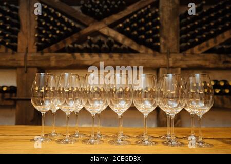 Rangée de verres brillants élégants sur une table en bois cave à vin avec bouteilles de vin sur étagères en arrière-plan Banque D'Images