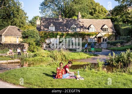 Visiteurs appréciant la lumière du soleil en soirée à côté de la ford de l'autre côté de la rivière Eye dans le village de Cotswold d'Upper Slaughter, Gloucestershire Royaume-Uni Banque D'Images