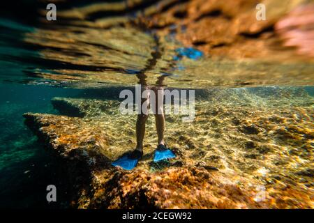 Croiser les jambes d'un garçon portant des palmes debout sur la pierre sous eau de mer Banque D'Images