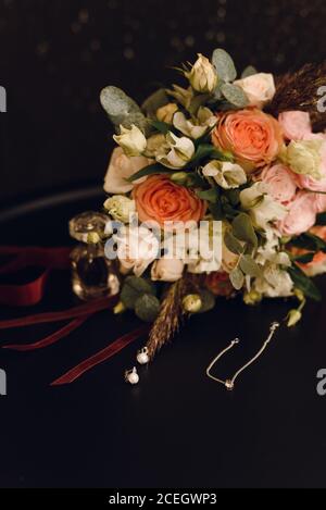 Mariage bouquet de roses à côté des bijoux de la mariée - uepochki et boucles d'oreilles sur velours rouge. Concept mariage et amour. Banque D'Images