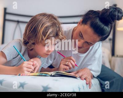 Belle femme et enfant mignon couché sur un lit confortable et coloriage des photos dans le carnet ensemble. Banque D'Images