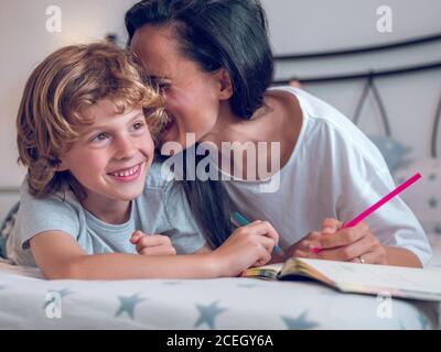 Belle femme et enfant mignon couché sur un lit confortable et coloriage des photos dans le carnet ensemble. Banque D'Images