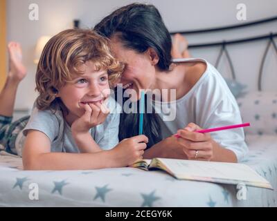 Belle femme et enfant mignon couché sur un lit confortable et coloriage des photos dans le carnet ensemble. Banque D'Images