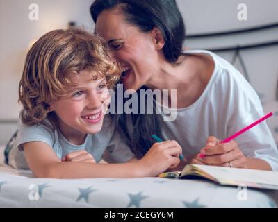 Belle femme et enfant mignon couché sur un lit confortable et coloriage des photos dans le carnet ensemble. Banque D'Images