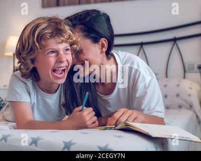 Belle femme et enfant mignon couché sur un lit confortable et coloriage des photos dans le carnet ensemble. Banque D'Images