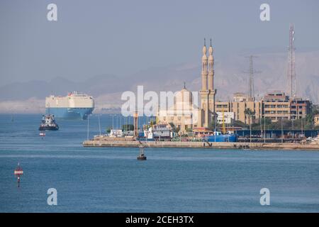 Égypte, Canal de Suez. Navires entrant dans le canal de Suez avec la mosquée au loin. Banque D'Images