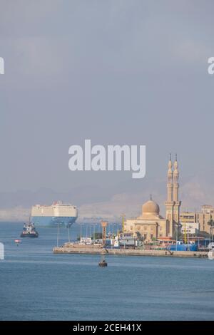 Égypte, Canal de Suez. Navires entrant dans le canal de Suez avec la mosquée au loin. Banque D'Images