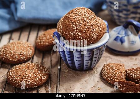 Petits gâteaux aux flocons d'avoine frais avec graines de sésame dans une tasse. Biscuits aux croustilles de sésame sur la grille pour la cuisson et thé bleu sur la table. Préparation pour le thé Banque D'Images