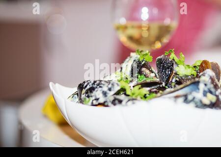 Moules cuites à la vapeur dans une sauce au fromage. Moules en coquilles dans le bol avec vin blanc sur la table. Banque D'Images