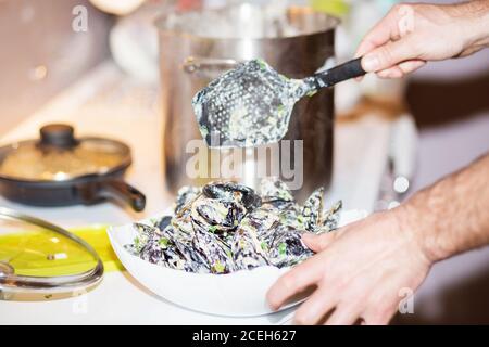 Moules cuites à la vapeur dans des coquilles dans le bol avec du vin blanc sur la table. Chef cuisant les moules dans la sauce au fromage. Banque D'Images