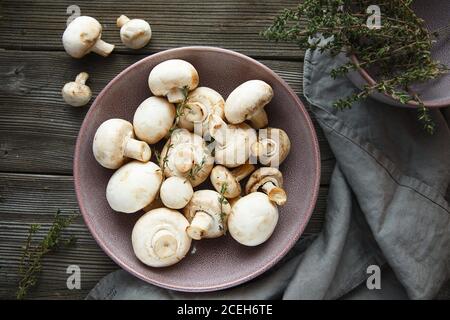 Champignons frais au thym. Champignons blancs frais champignon dans un bol violet sur fond de bois. Banque D'Images