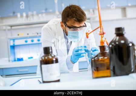 Beau chercheur en vêtements de travail de protection debout dans le laboratoire et flacon d'analyse avec liquide Banque D'Images