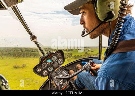 Jock au bâton de contrôle de son hélicoptère Robinson R44 Raven dans le territoire du Nord, en Australie Banque D'Images