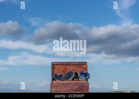 Une caisse en bois contenant trois montres-bracelets, contre un beau ciel bleu avec des nuages Banque D'Images