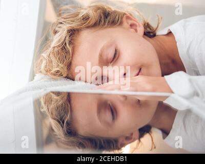 Adorable garçon avec des cheveux ondulés couché près de la table moderne et sommeil paisible Banque D'Images