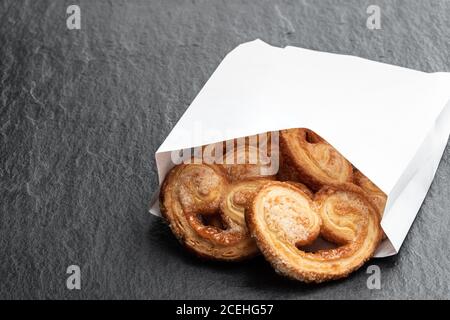 Cœur de pâte feuilletée émaillé de sucre caramélisé dans un sac en papier sur fond de pierre noire Banque D'Images