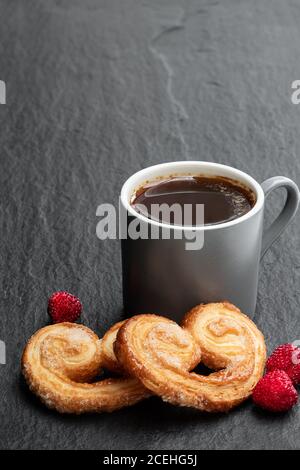 Cœur de pâte feuilletée émaillé de sucre caramélisé et d'une tasse de café sur fond de pierre noire Banque D'Images