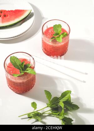 Deux verres de smoothie frais rouge melon d'eau avec des pailles à boire à la menthe et au papier sur une table blanche. Prise de vue en hauteur avec espace de copie. Minimalisme. Banque D'Images