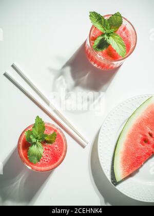 Deux verres de smoothie frais rouge melon d'eau avec des pailles à boire à la menthe et au papier sur une table blanche. Prise de vue en hauteur avec espace de copie. Minimalisme. Banque D'Images
