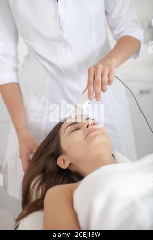 Femme aux cheveux foncés allongé sur le canapé tout en ayant une peau au laser soins dans le salon Banque D'Images