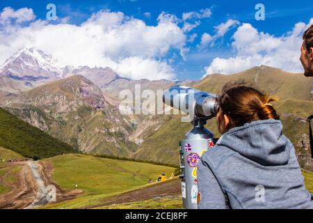 Femme et homme regardant dans le binoscope dirigé vers la neige Sommets de la montagne de Kazbeg depuis le point de vue de la Trinité de Gergeti Église Tsminda Sameba Sainte Banque D'Images