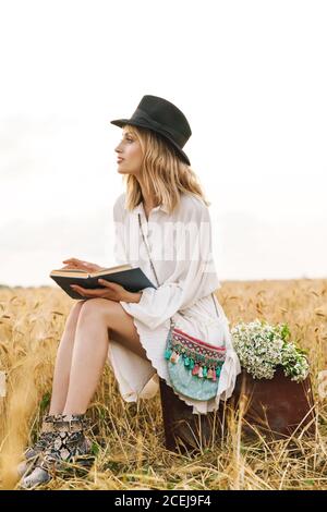 Image d'une jeune femme blanche blonde lisant un livre en étant assise dans le champ doré sur la campagne Banque D'Images