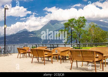 Belle vue depuis la terrasse du café donnant sur les hautes montagnes et le lac de Côme. Des chaises de restaurant vides en osier attendent les clients dans un Banque D'Images