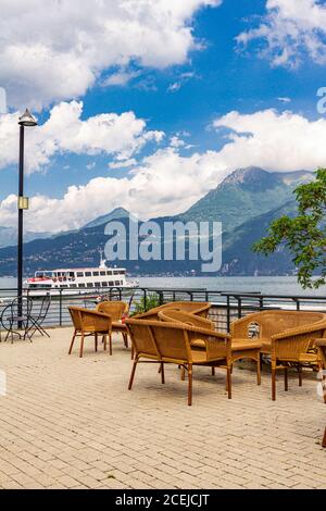 Belle vue depuis la terrasse du café donnant sur les hautes montagnes et le lac de Côme. Des chaises de restaurant vides en osier attendent les clients dans un Banque D'Images