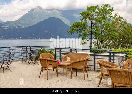 Belle vue depuis la terrasse du café donnant sur les hautes montagnes et le lac de Côme. Des chaises de restaurant vides en osier attendent les clients dans un Banque D'Images