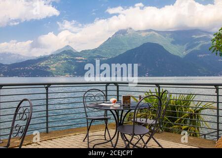 Belle vue depuis la terrasse du café donnant sur les hautes montagnes et le lac de Côme. Des chaises de restaurant vides en osier attendent les clients dans un Banque D'Images